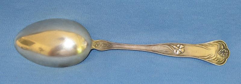 Souvenir Placer Mining Spoon Reverse Nome Alaska.JPG - SOUVENIR MINING SPOON NOME ALASKA - Sterling silver souvenir spoon, engraved mining scene in bowl showing miners panning for gold, marked PLACER MINING, NOME, decorative design with flowers on handle, reverse marked Sterling with makers mark, 5 3/8 in. long  [The Nome mining district is a gold mining district in Alaska. It was discovered in 1898 when Erik Lindblom, Jafet Lindeberg and John Brynteson, the "Three Lucky Swedes", found placer gold deposits on Anvil Creek and on the Snake River, a few miles from the future site of Nome. News of the strike reached the gold fields of the Klondike that winter and by 1899 Anvil City, as the new camp was called, had a population of 10,000. It was not until gold was discovered in the beach sands in 1899 and news reached the outside that the real stampede was on. Thousands poured into Nome during the spring of 1900, as soon as steamships from the ports of Seattle and San Francisco could reach the north through the ice. In the treeless location, tents soon covered the landscape, reaching the water's edge, and extending most of the 30 miles between Cape Rodney and Cape Nome. Buildings of finished board lumber began going up as early as 1899, as soon as ships reached Nome from the states with supplies.  The town was locally known as Anvil City for much of 1899, but the United States Post Office Department insisted on calling the community Nome, apparently because it was thought that a town called Anvil City would be easily confused with the village of Anvik on the lower Yukon. A vote was held and the town’s merchants reluctantly agreed to change the name from Anvil City to Nome.  This was one of the first and was the biggest Alaskan gold rush in North America; only the California and Klondike stampedes were larger. A chaotic and lawless scene ensued, with rampant claim-jumping, crooked judges, and not enough gold found for the 20,000 prospectors, gamblers, shop and saloon-keepers, and prostitutes living in the tent city on the beachfront tundra, at least not at first. Then someone thought to pan the red-and-black streaked beach sands. Within days, gold was found for tens of miles up and down the beach from Nome. More than a million dollars' worth of gold was taken from the beach in 1899. Subsequently the second and third beach lines were discovered and mined. Anvil Creek produced the second-largest gold nugget found in Alaska (182 troy ounces).  Except while prohibited by law during WWII, placer mining near Nome has continued to this day. Over 3.6 million troy ounces of gold have been recovered from the creeks of the Nome District.  A myriad of small hard-rock gold deposits were exploited near Nome, but production was very small, compared to the placer deposits, and none of the hard rock mines operated for more than a few years.]